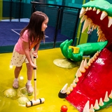A girl aiming the ball towards a giant alligator statue's mouth.