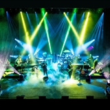 Band playing on a stage with blue and green lights.