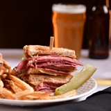 Reuben sandwich with fries and beer in the background.