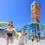 Two girls playing at an outdoor waterpark with tall waterslide behind.