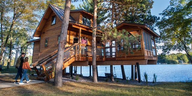 Large treehouse above the ground overlooking a lake.