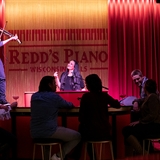 A man plays violin to guests at the piano bar.