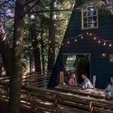 People on a vacation rental home deck surrounded by wooded forest area.