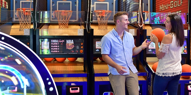 A couple plays a basketball arcade game.